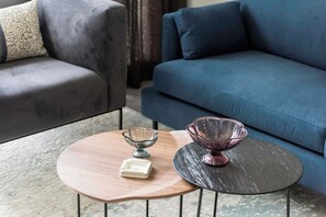 Een woonkamer met een blauwe bank, een houten salontafel en twee glazen schalen.