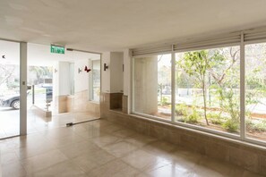 A spacious indoor area with large windows, a tiled floor, and a visible exit sign.
