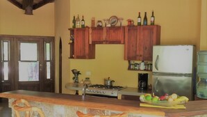 Une cuisine avec des meubles de rangement en bois, un réfrigérateur, une cuisinière et un coin bar avec des tabourets.