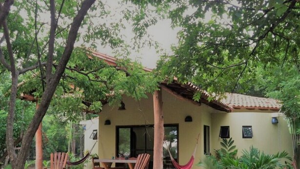 Une petite maison de plain-pied dotée d’un patio, d’un hamac et d’une table à manger avec des chaises.