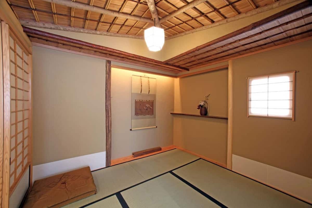 Une pièce de style japonais traditionnel, avec un sol recouvert de tatamis, une porte coulissante en papier de riz (shoji), un luminaire suspendu et une petite étagère sur laquelle est posé un vase.