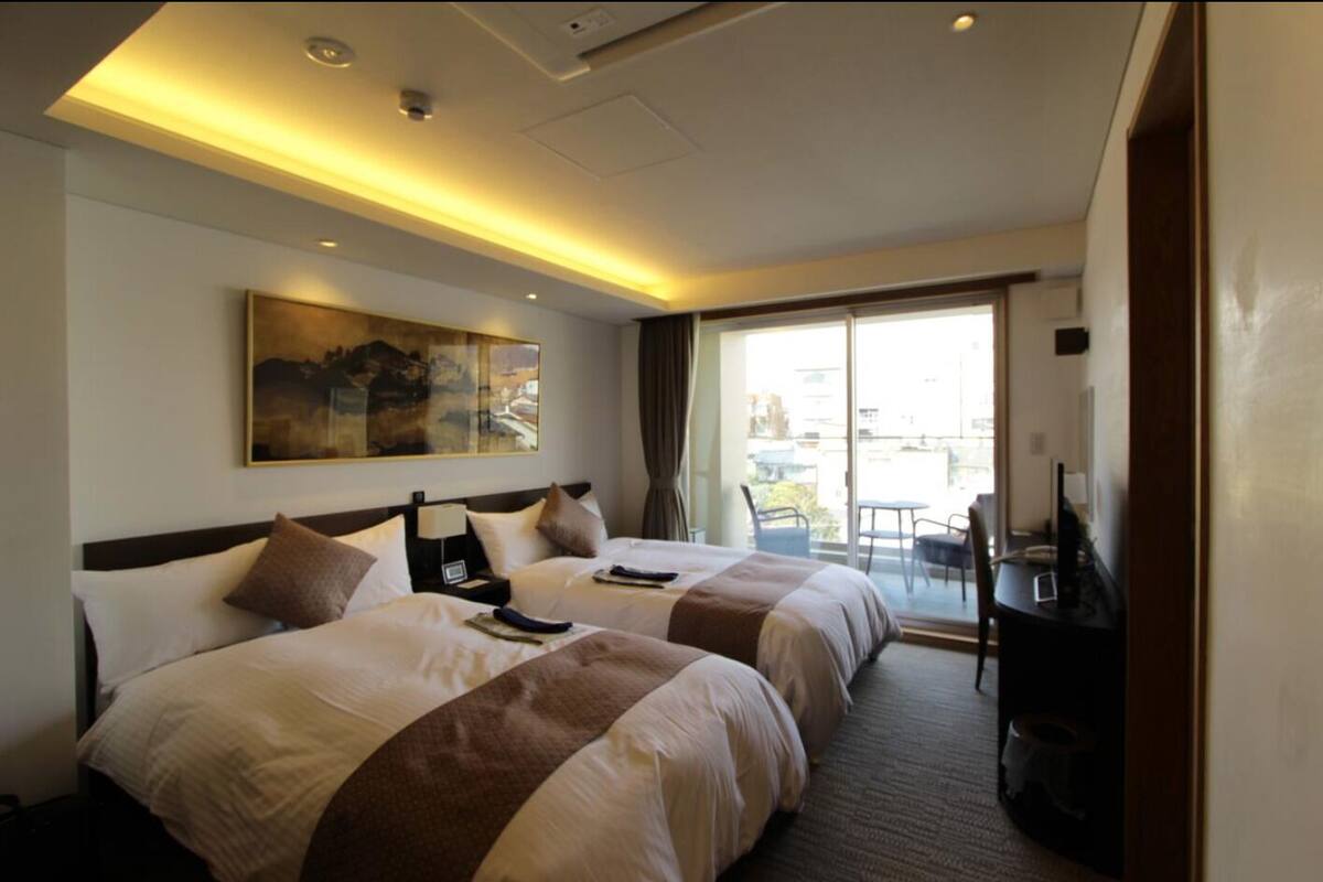 Une chambre d’hôtel avec deux lits, un tableau au mur, une télévision et un balcon avec des meubles d’extérieur.