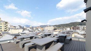 A rooftop terrace with concrete tables and benches, offering a view of a cityscape and mountains in the distance. - Hana Touro Hotel Gion (Kyoto)