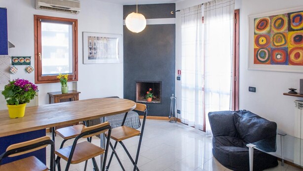 Un salon moderne avec une cheminée, un coin repas avec une table et des chaises en bois, et un grand tableau abstrait accroché au mur.