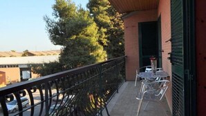 Un balcon avec une balustrade en métal, une table avec des chaises et un pot de fleurs.