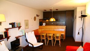 A living room with a red sofa, a wooden dining table with chairs, a television, and bookshelves.