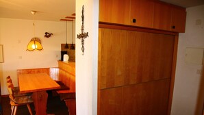 A wooden dining table with chairs, a hanging lamp, and a wooden cabinet.