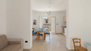 Un salon moderne avec un canapé, un coin repas comprenant une table et des chaises, et une cuisine en arrière-plan.