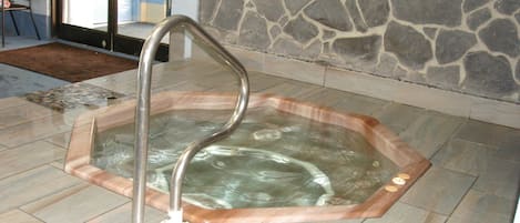 Ein Whirlpool mit Metallleiter, Steinwand und gefliestem Boden.