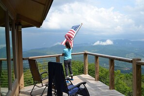 Une terrasse en bois offrant une vue sur les montagnes, et une personne tenant un drapeau américain.