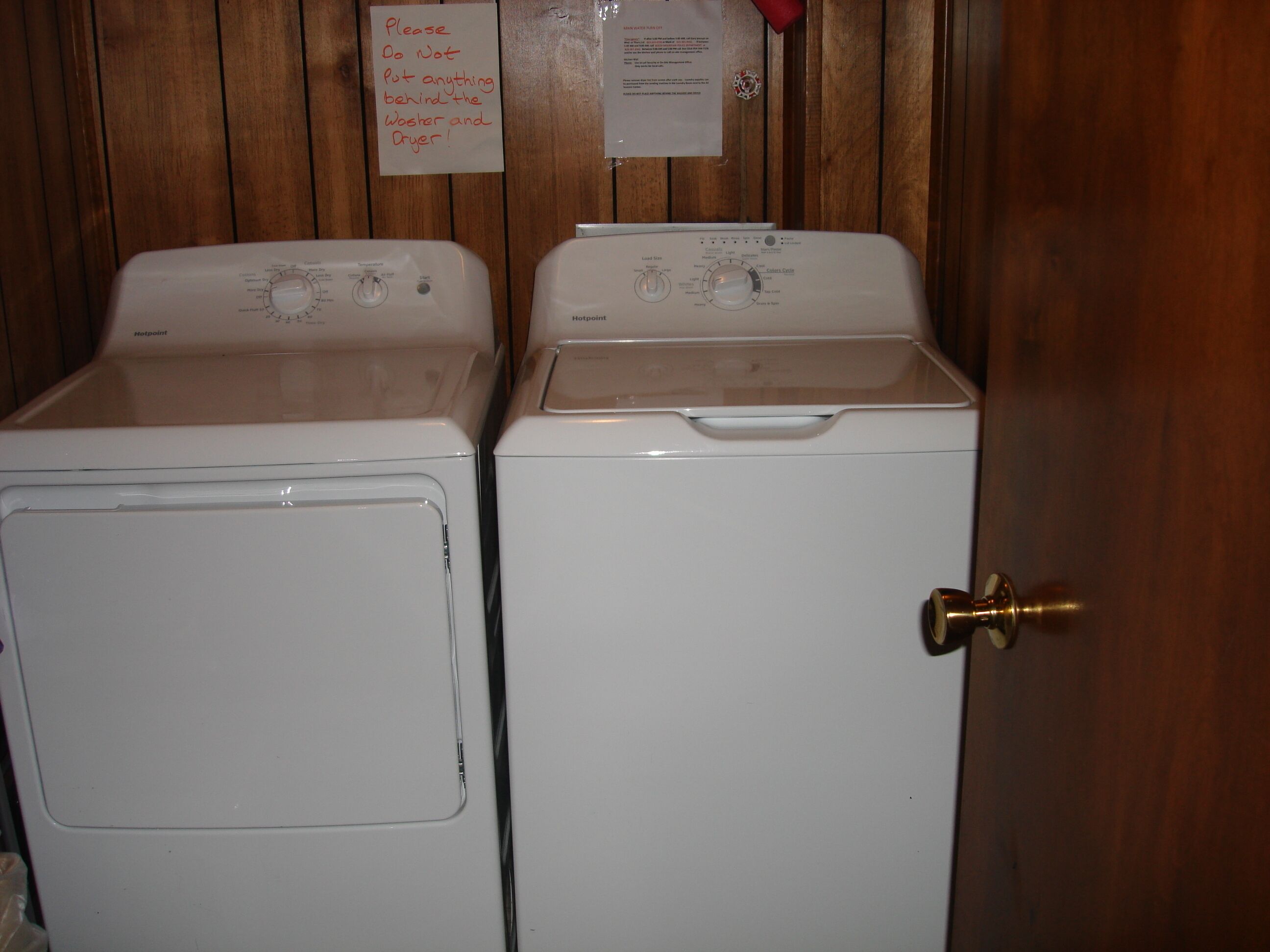 Deux machines à laver blanches dans une pièce en bois avec une porte.