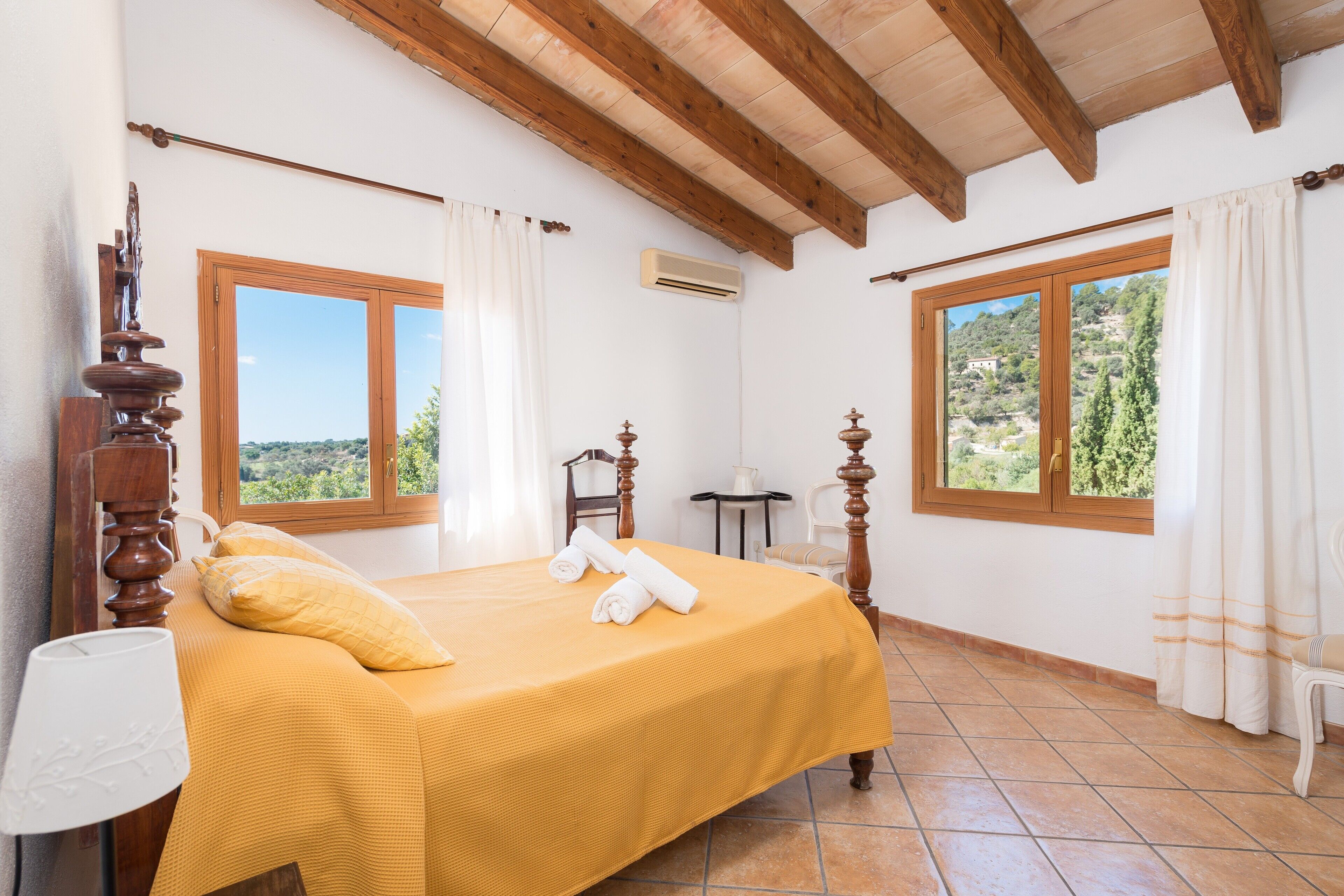 Une chambre à coucher avec un lit, deux fenêtres, une chaise, une table et une lampe.