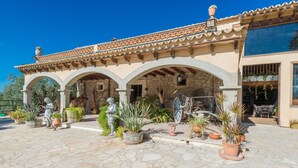 Un pati amb paviment de pedra, un porxo cobert amb arcs, plantes en testos i mobiliari exterior.