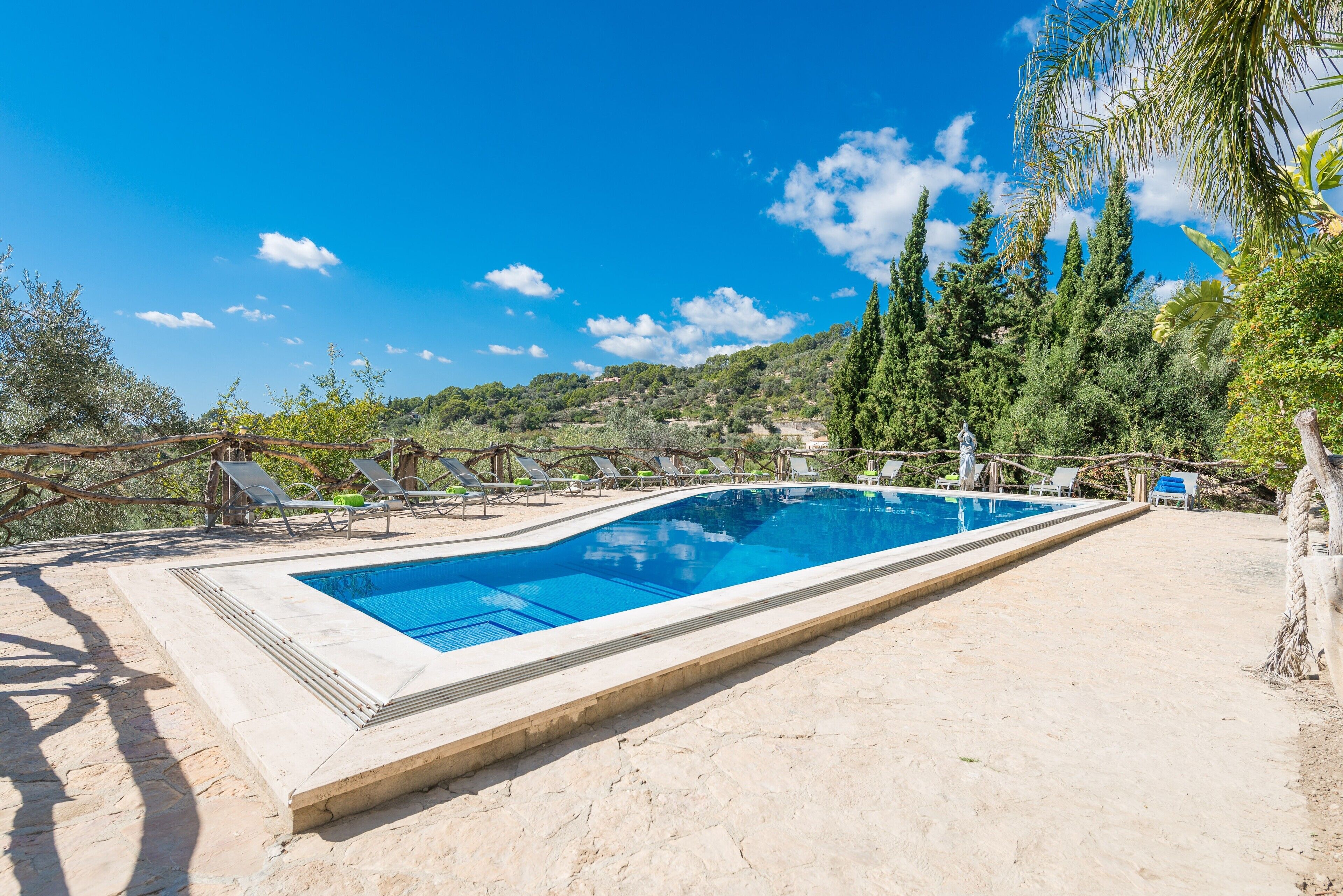 Una piscina rectangular con borde de azulejos, rodeada por una zona de arena y protegida por árboles.