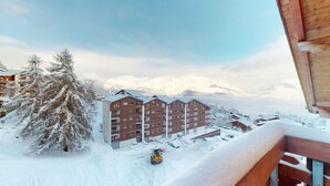 Een meerhoog gebouw met een met sneeuw bedekte dak en een helder uitzicht op besneeuwde bergen op de achtergrond.