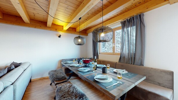 Een eethoek met een houten tafel voor vier personen, een bank en een raam met gordijnen.