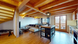 Een gezellig, goed verlicht loft-appartement met een houten plafond, een bank, een eettafel en een keukenhoek.
