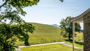 Une maison avec un porche, une pelouse et une colline en arrière-plan.