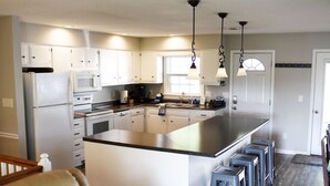 Une cuisine moderne avec des armoires blanches, un grand îlot central, des tabourets de bar et des luminaires suspendus.
