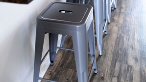 Une cuisine avec un plancher en bois, un comptoir foncé et trois tabourets gris.