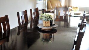 Une table à manger avec des chaises, une petite plante et une lampe dans une pièce où se trouvent un canapé et une fenêtre.