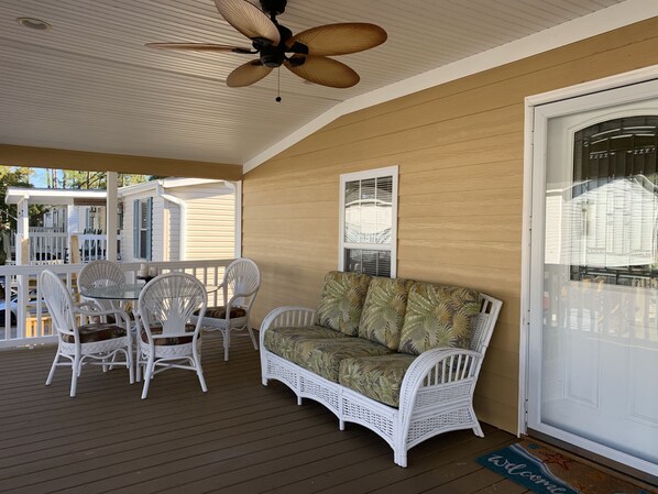 A covered porch with a ceiling fan, white wicker furniture, and a cushioned sofa.