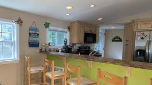 A kitchen with a green accent wall, wooden bar stools, a microwave, and a refrigerator. - SNOW BIRDS..SPECIAL RATES FOR WINTER TRAVELS - A Fun, Sun N' Surfin' Kinda Place (Murrells Inlet)