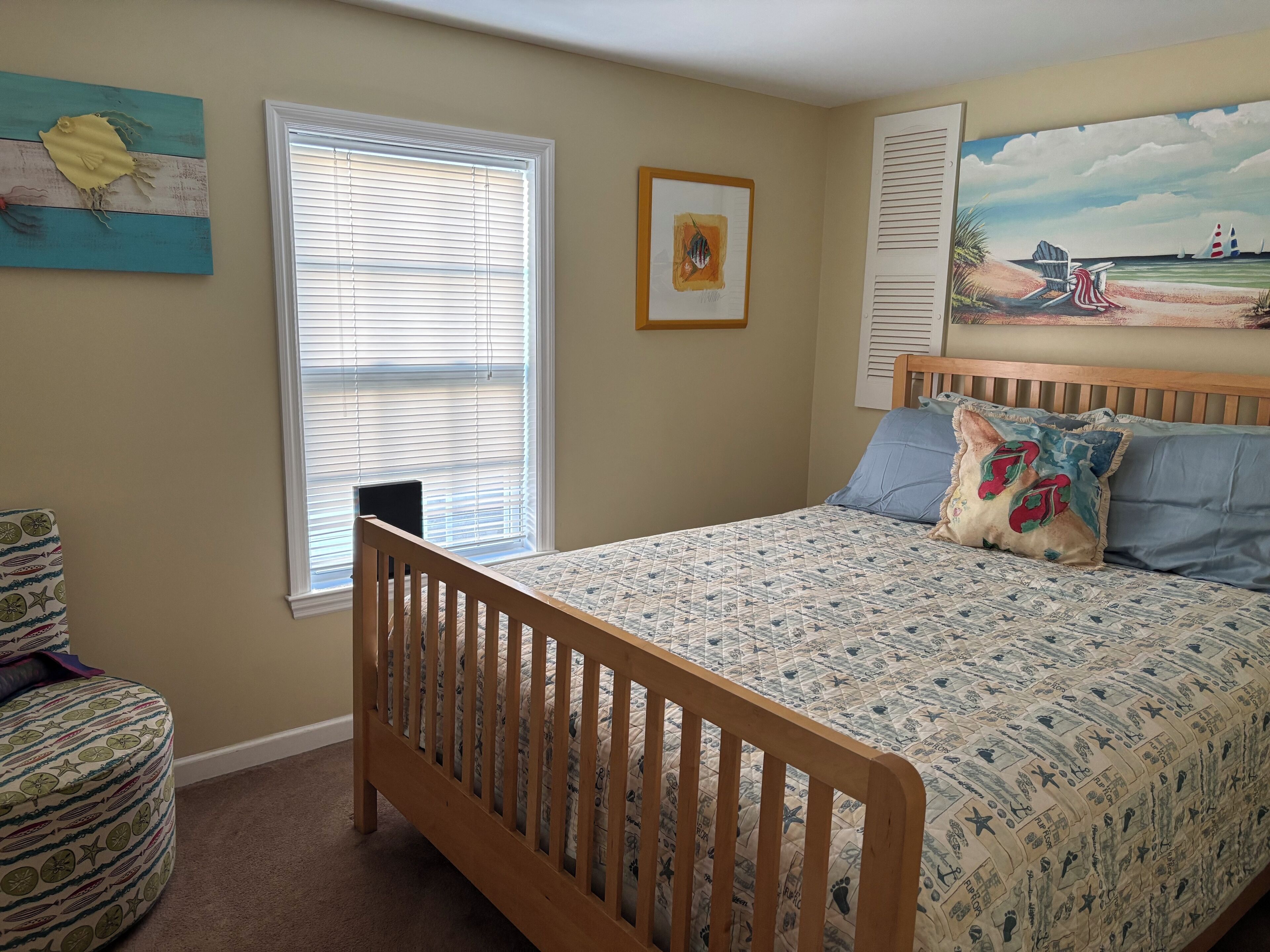 Une chambre avec un lit en bois, une fenêtre avec des stores, une chaise et un tableau accroché au mur.