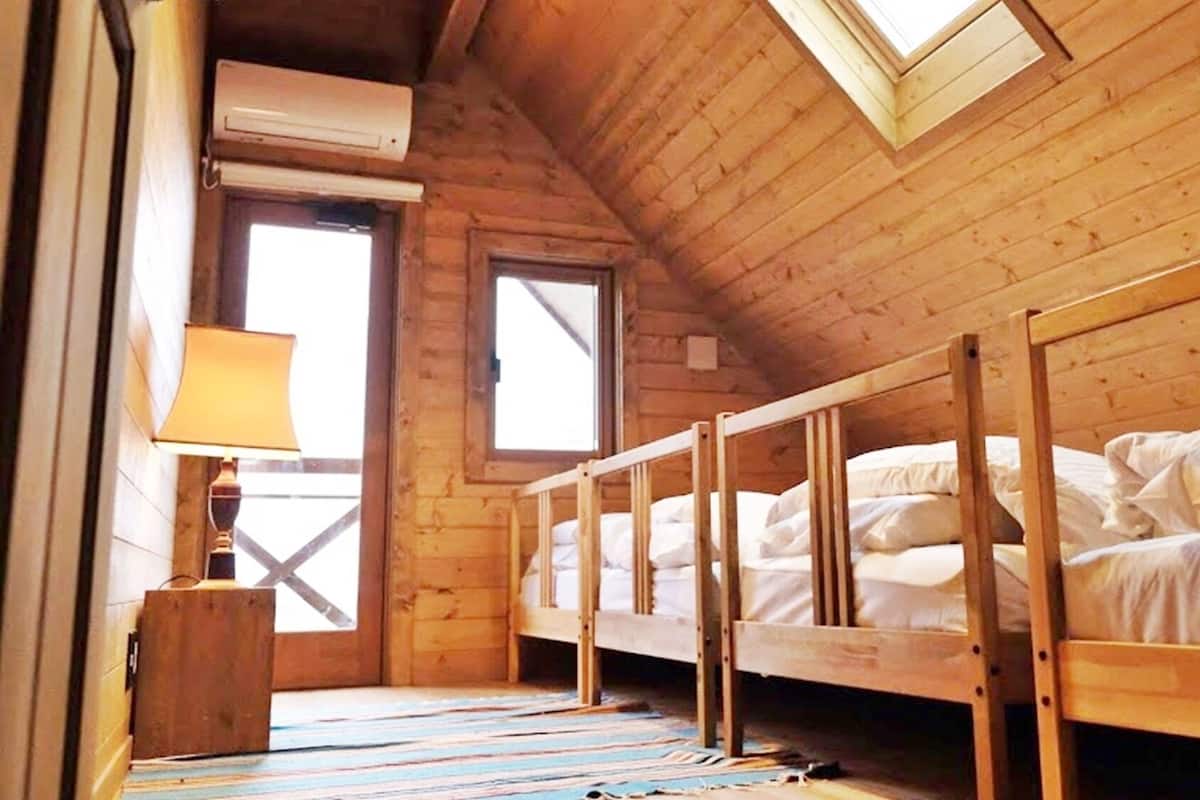 A wooden cabin room with bunk beds, a window, and a lamp.