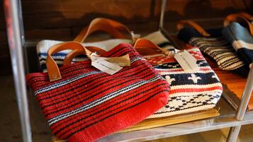 Une collection de sacs tissés, chacun muni d’une étiquette, est exposée sur une étagère en métal.