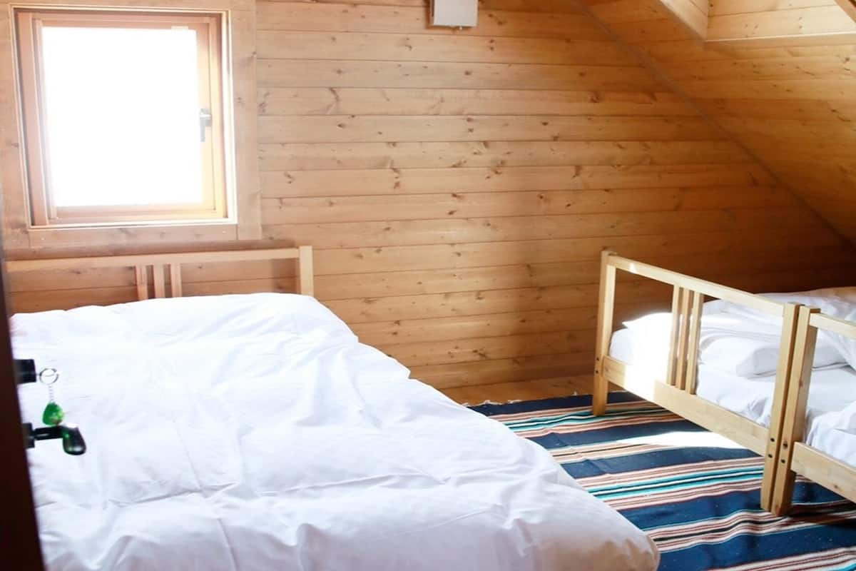 A small, wooden cabin room with two beds, a window, and a striped rug.
