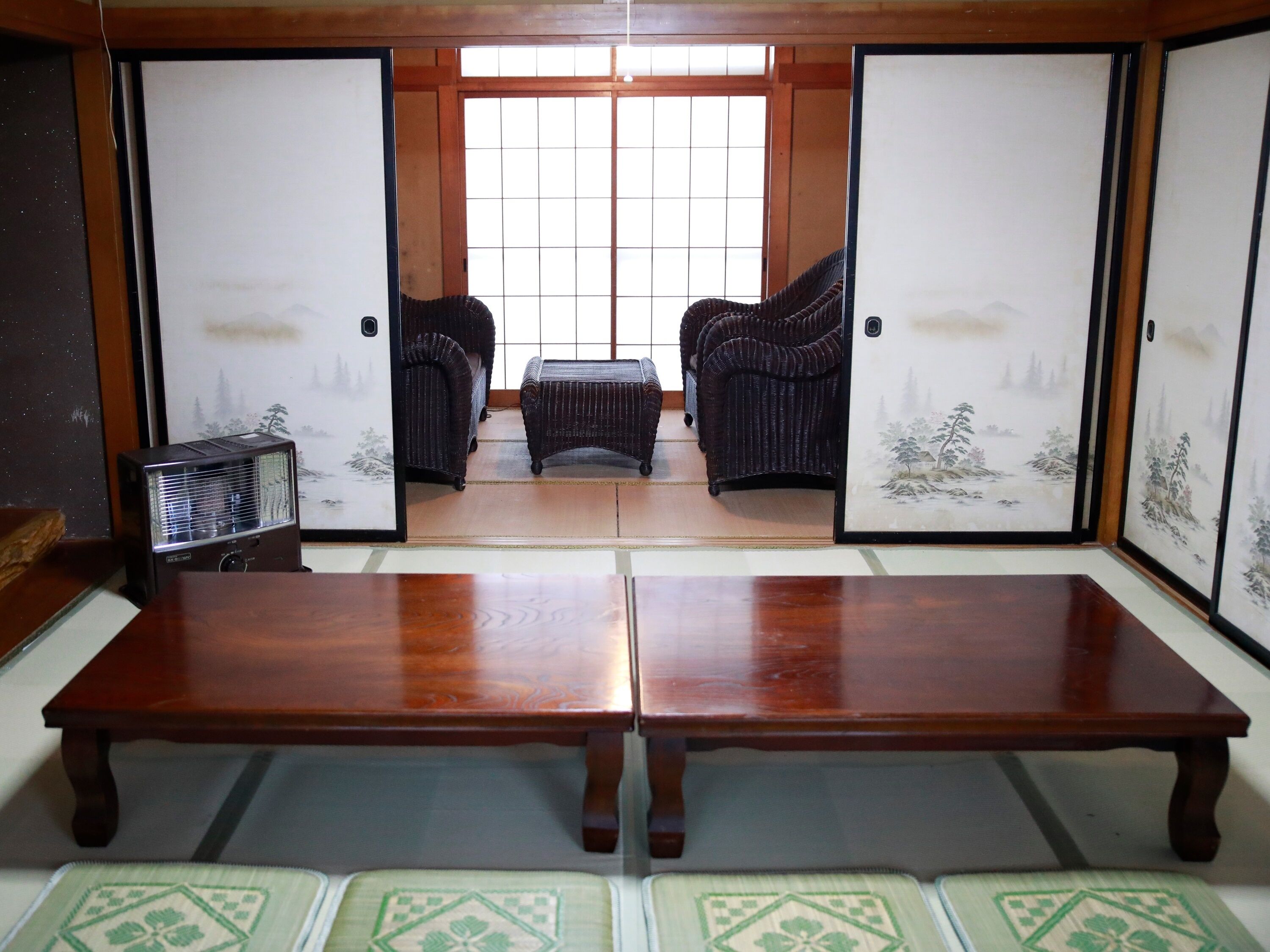 Ein traditioneller japanischer Raum mit Tatami-Bodenbelag, einem niedrigen Holztisch und zwei Tatami-Matten mit Kissen.