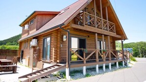 Una cabaña de madera con balcón, una escalera que lleva a la entrada y un patio con mobiliario exterior.
