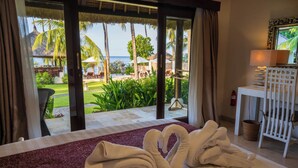 A hotel room with a bed, a view of a tropical garden and the sea, and a small table with a lamp. - Kubu Indah Dive & Spa Resort (Kubu)