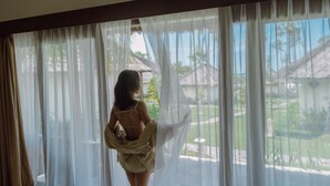 A room with sheer curtains, a view of a garden, and a house in the background. - Kubu Indah Dive & Spa Resort (Kubu)