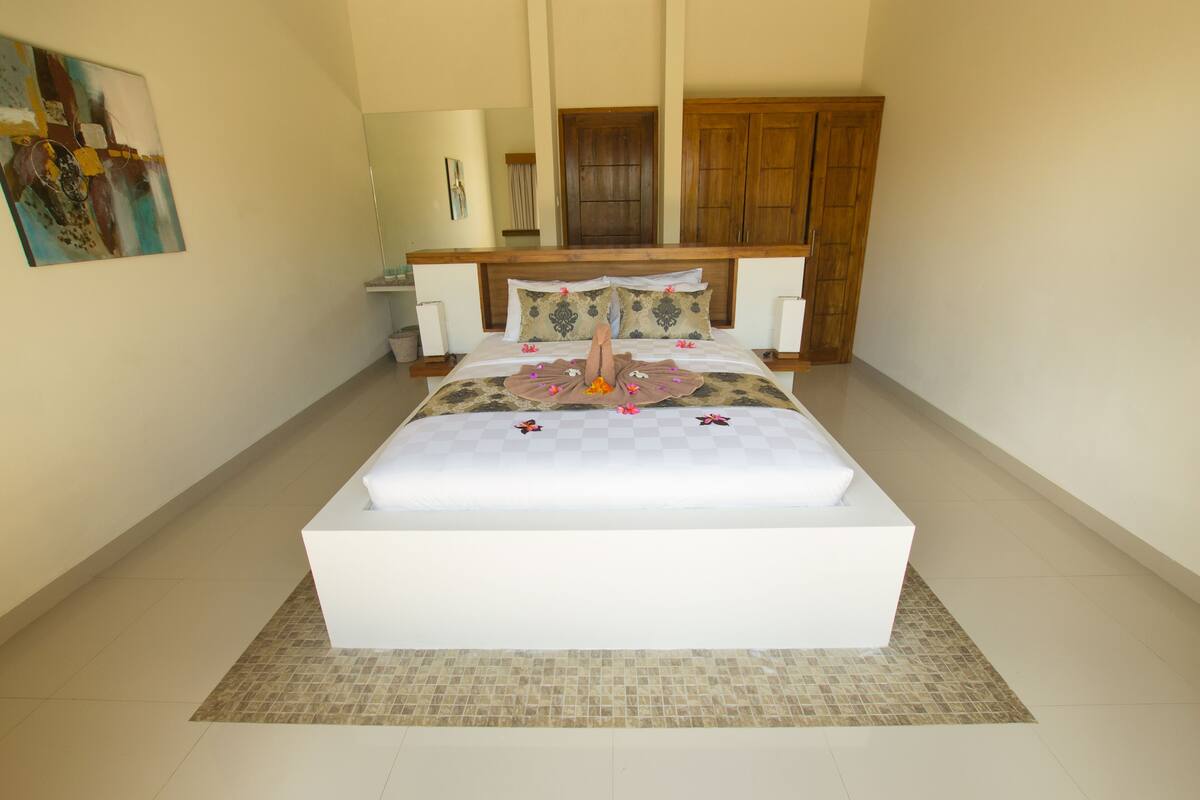 A spacious bedroom with a large bed, wooden headboard, and a small bedside table.