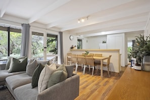 Ein modernes Wohnzimmer mit einer Couch, einem Esstisch und Stühlen. Es gibt eine Küchenzeile mit Schränken und einem Kühlschrank.