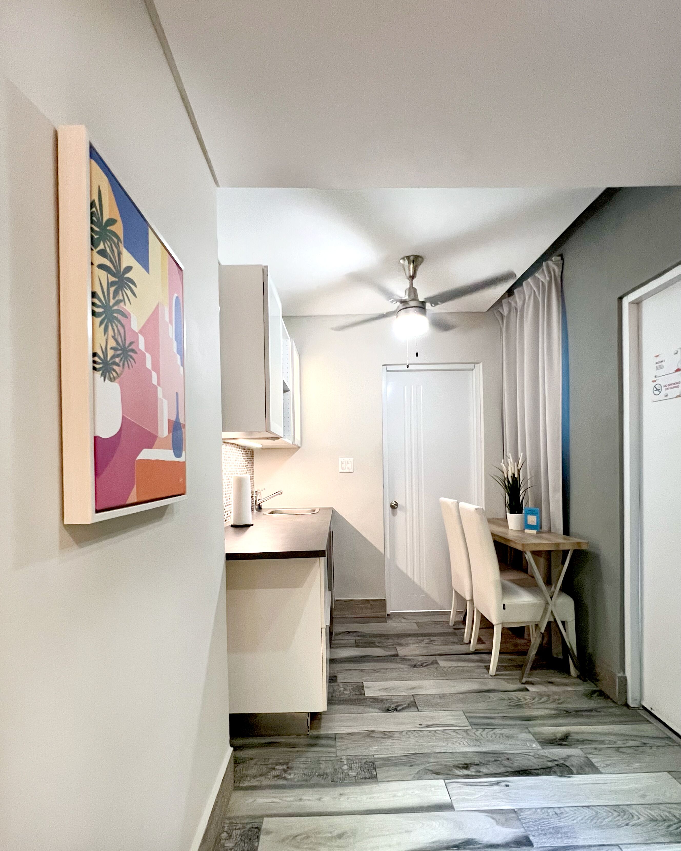 A compact kitchen with a dining area, a ceiling fan, and a door leading to another room.