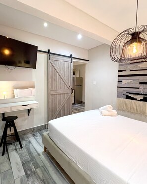 A modern bedroom with a bed, a desk, a TV, and a unique light fixture. - Tapia Haus 103 (San Juan)