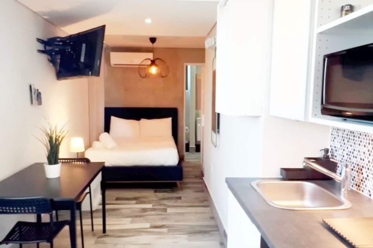Une chambre d’hôtel de taille réduite, comprenant un lit, une petite table à manger et un coin cuisine.
