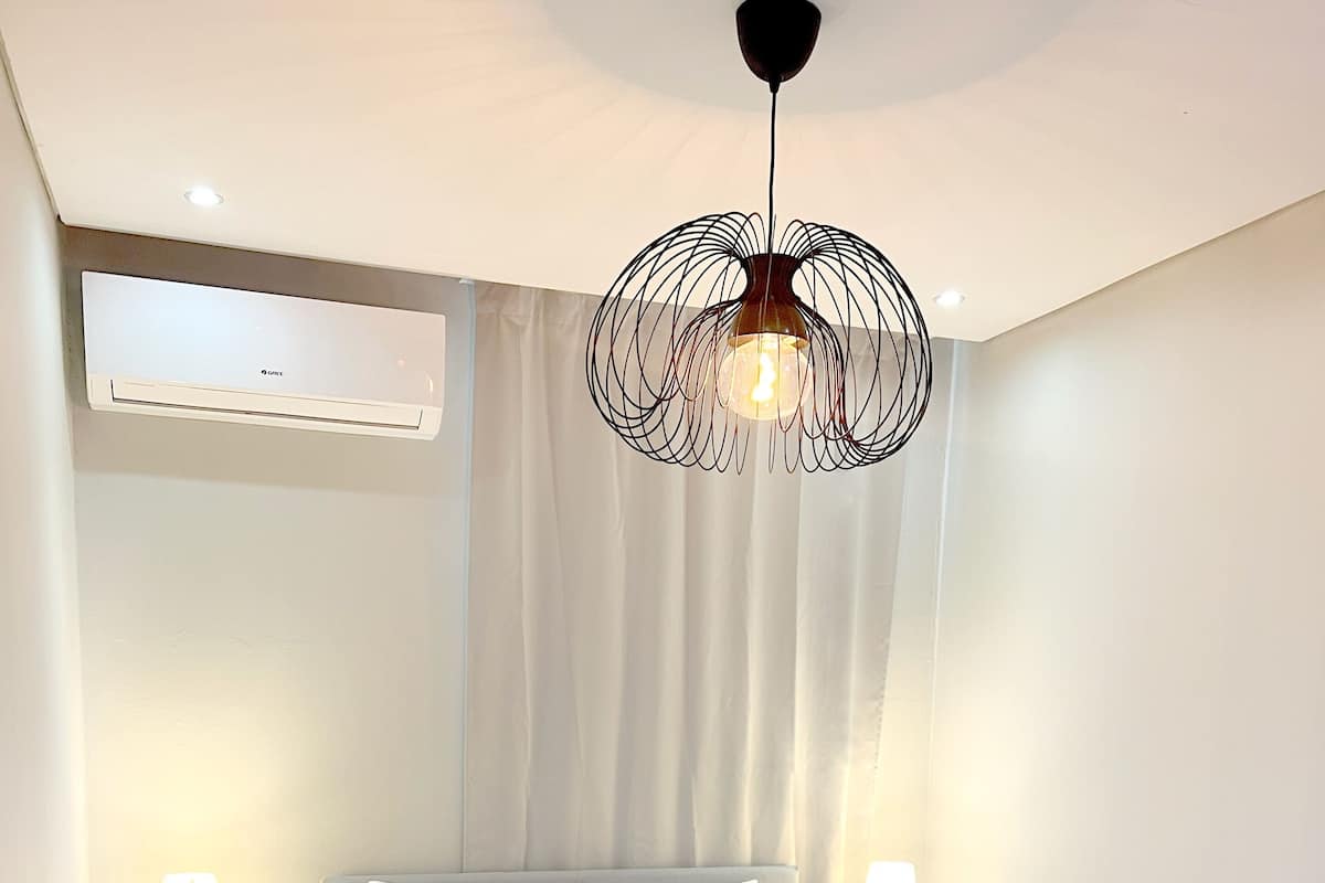 Une chambre moderne avec un grand lit, deux tables de chevet avec des lampes, un luminaire au plafond et un appareil de climatisation.