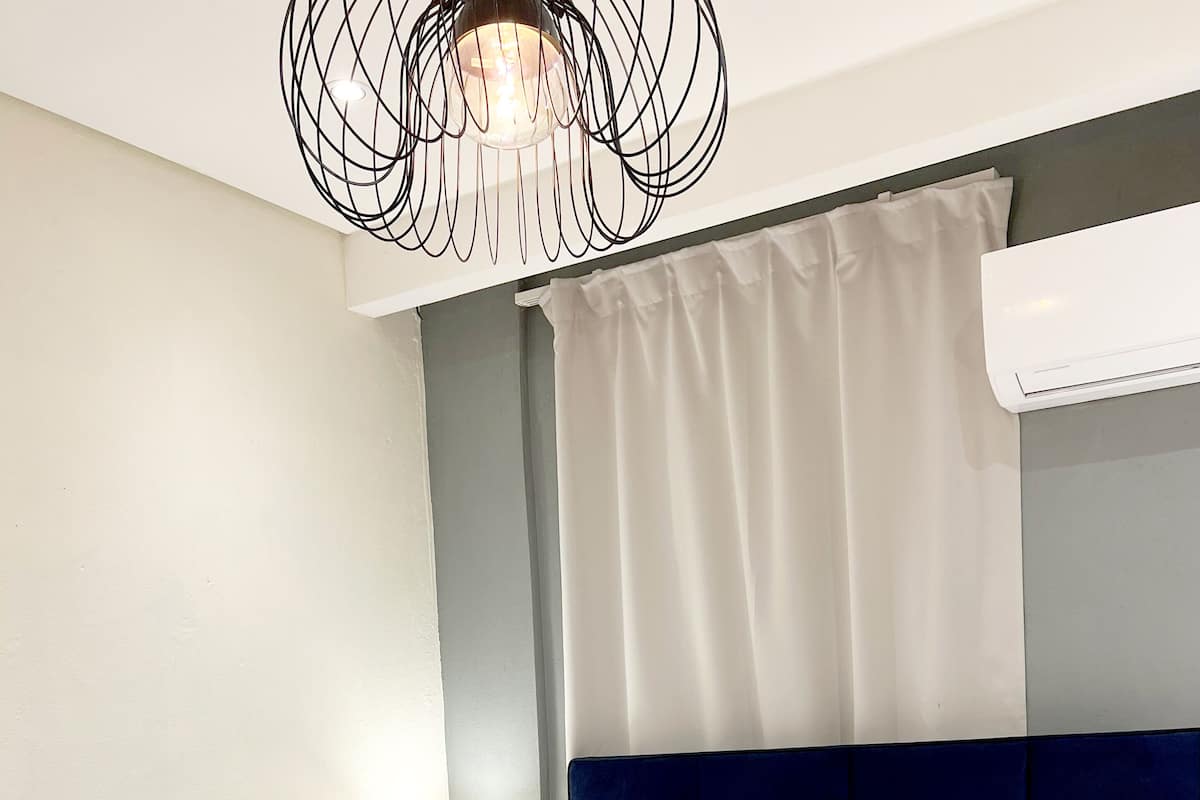 Un lit bien fait, avec du linge de lit blanc et une serviette enroulée, une lampe de chevet et un luminaire suspendu au design moderne.