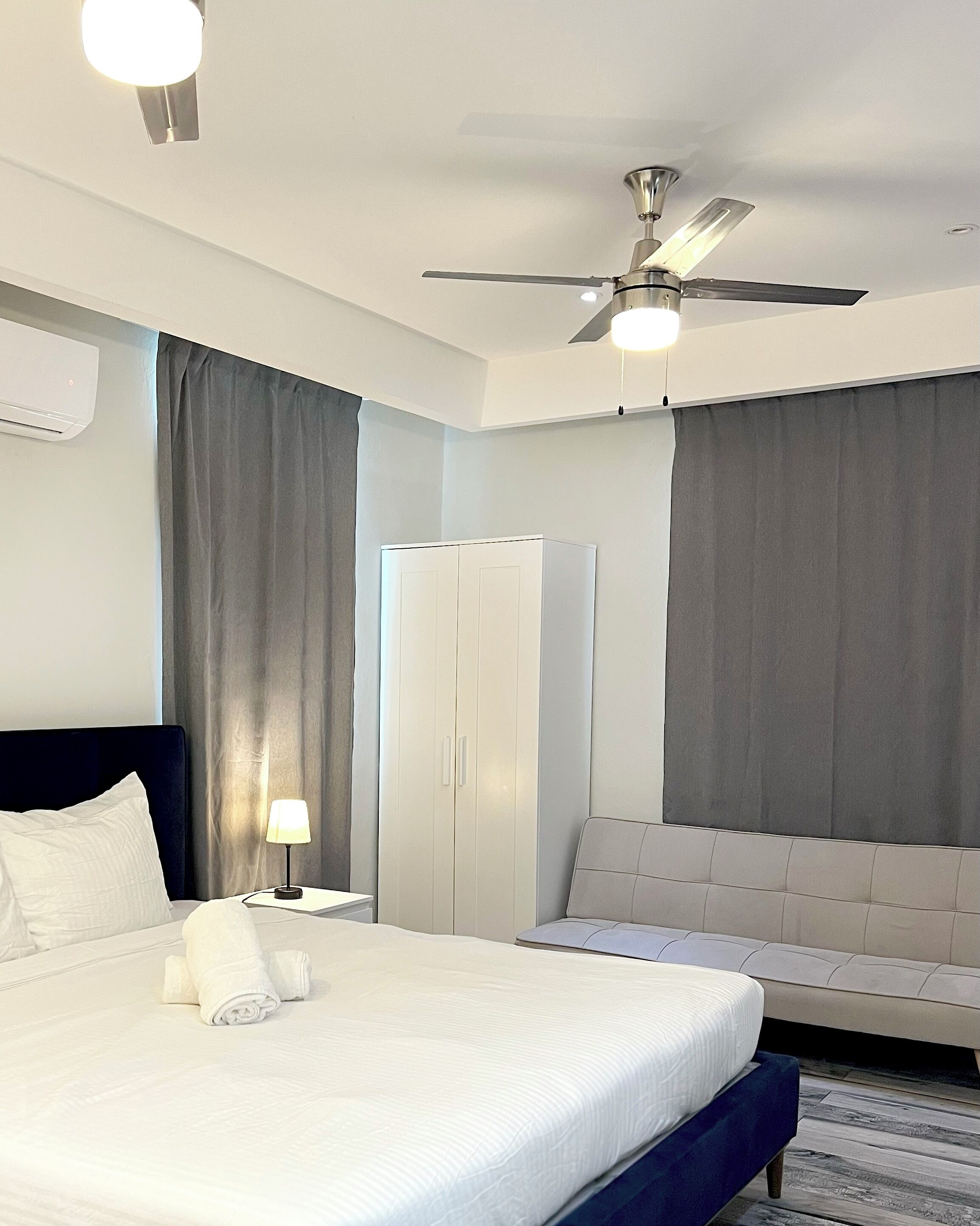 Ein Hotelzimmer mit Bett, Nachttisch, Lampe, Kleiderschrank und Deckenventilator.