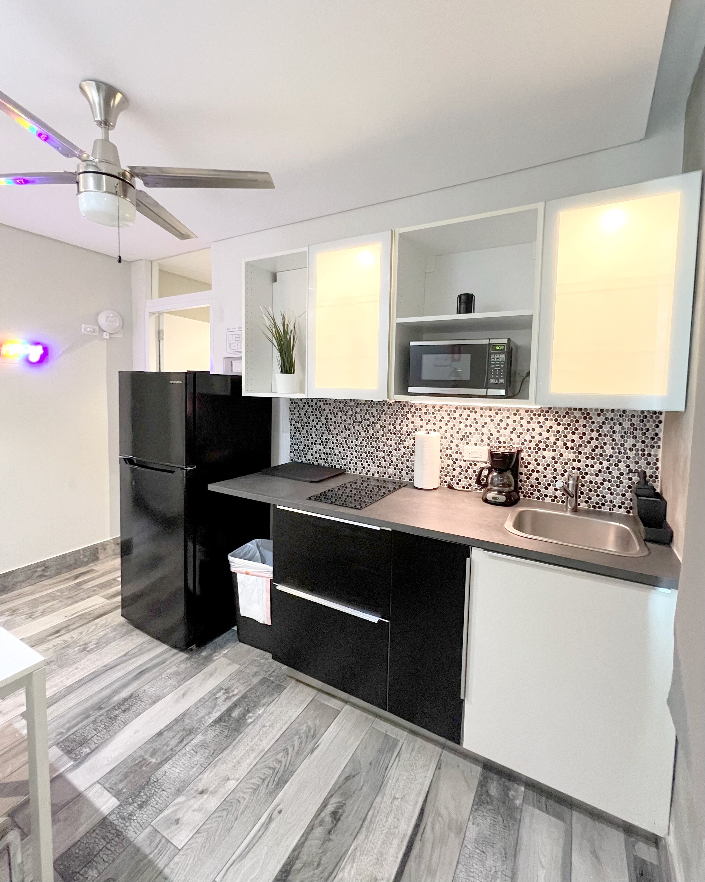 Une cuisine moderne avec un réfrigérateur noir, un four à micro-ondes, un évier et un ventilateur de plafond.