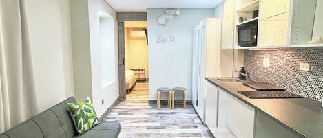 Un pasillo estrecho con un sofá y una kitchenette a un lado, y una puerta que da a otra habitación al otro.