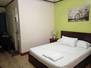 Een hotelkamer met een bed, een nachtkastje met lamp, een schilderij aan de muur en een deur naar een andere kamer.