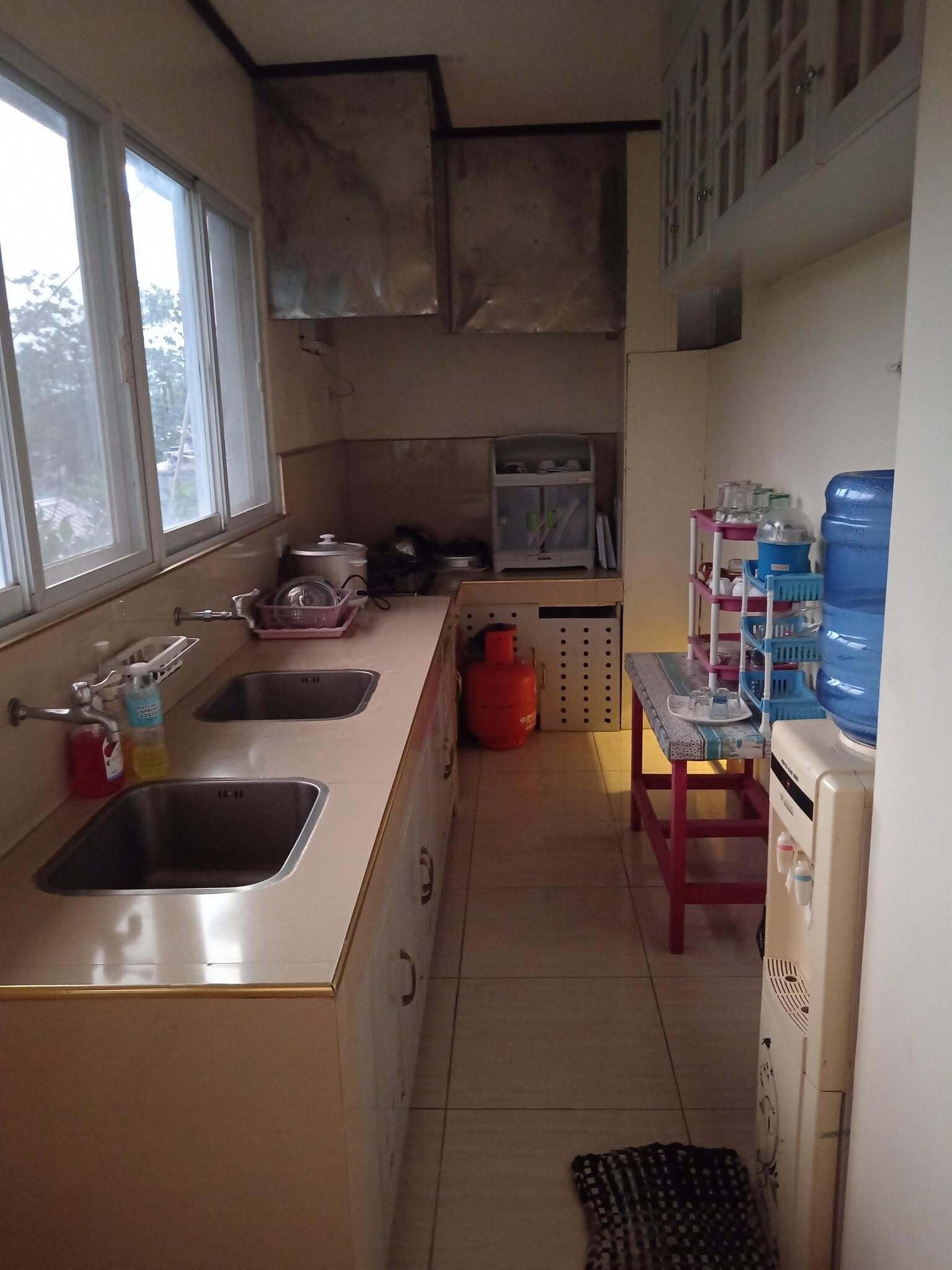 A kitchen with two sinks, a water dispenser, a gas cylinder, and a microwave.