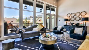 A modern living room with large windows, a sofa, armchairs, a coffee table, and a small side table.