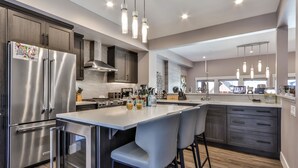 A modern kitchen with stainless steel appliances, a central island with bar stools, and pendant lighting.