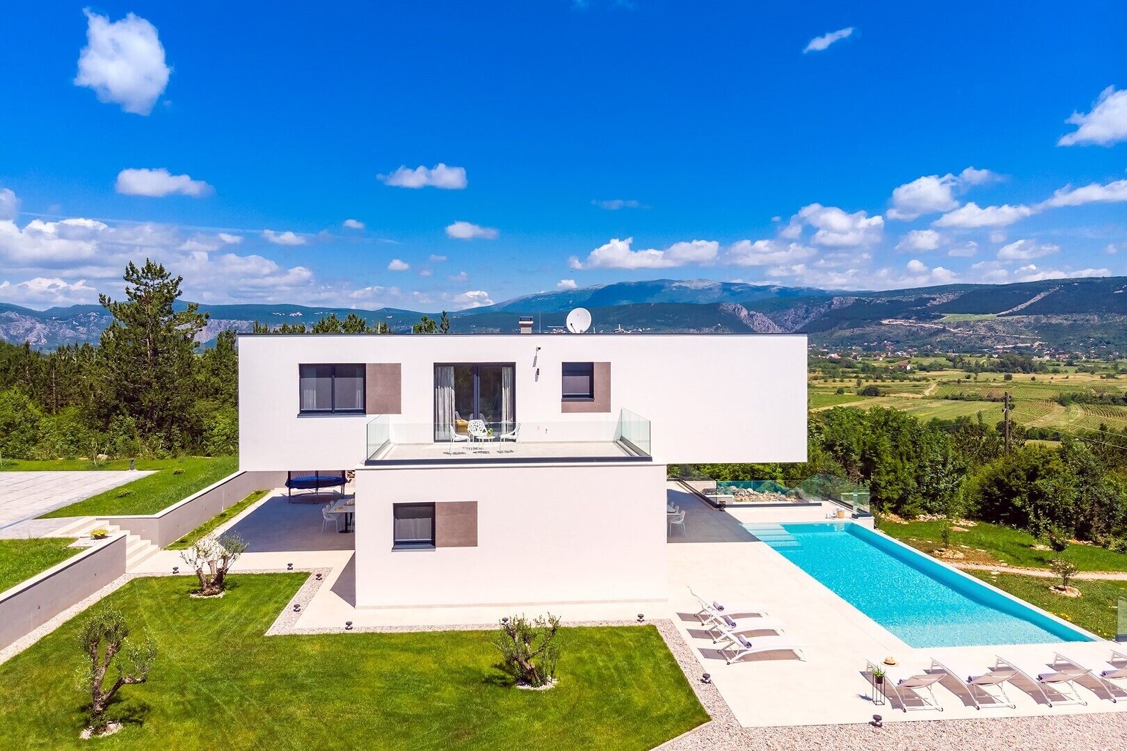 A modern two-story house with a swimming pool, surrounded by a well-maintained lawn and a scenic mountain view.